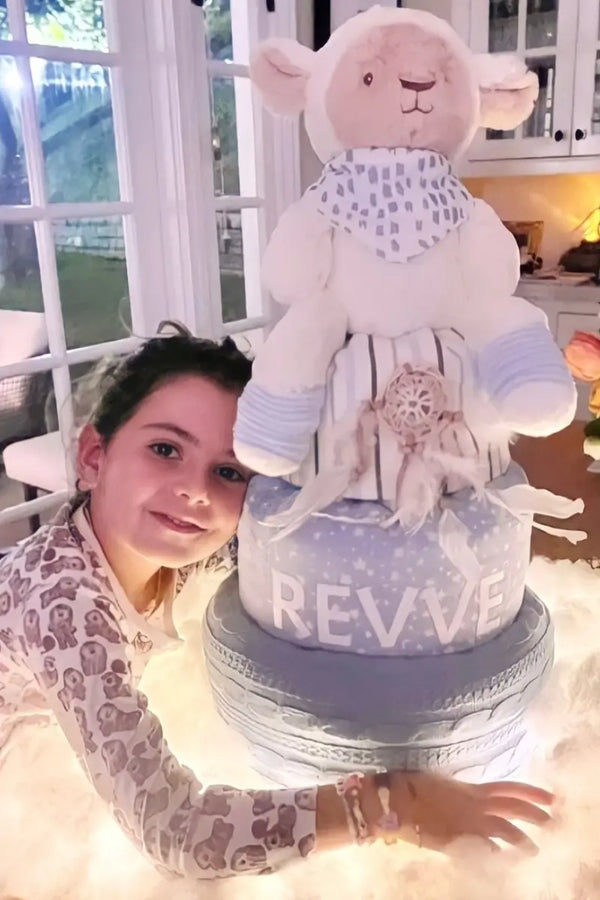Diaper cake for a gender reveal party featuring a plush lamb topper and soft pastel decorations.