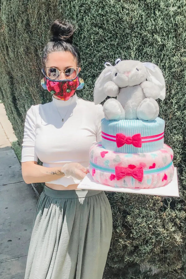 Diaper gift basket featuring a plush bunny atop a colorful two-tiered diaper cake with pink and blue bows.